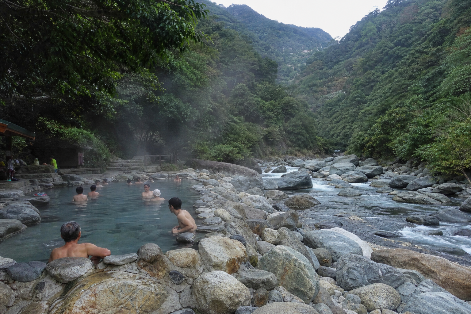 南勢溪畔的野溪溫泉，有泡湯民眾在天然石砌湯池中，蒸氣裊裊，背景是翠綠山林與溪谷